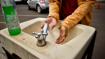person in orange jacket washing hand
